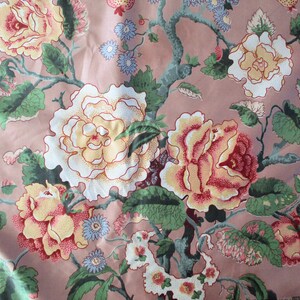 May include: A pink fabric with a floral pattern featuring white, yellow, and red roses with green leaves. The fabric has a vintage aesthetic.