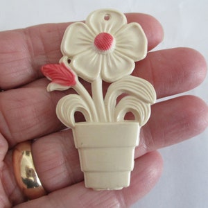 Peut inclure: Une fleur en plastique blanche avec un centre rouge dans un pot en plastique blanc. La fleur a un seul bouton et des feuilles.