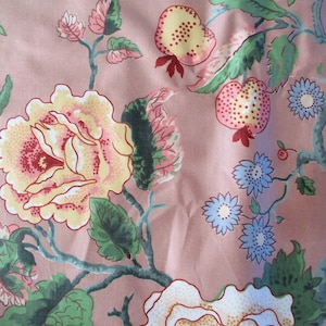 May include: A pink fabric with a floral pattern featuring yellow, red, and blue flowers, green leaves, and pink and yellow fruit.