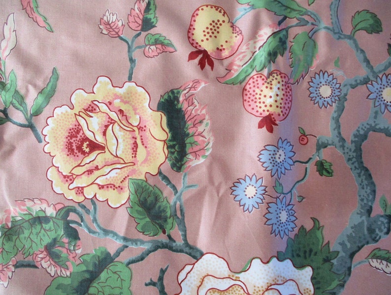 May include: A pink fabric with a floral pattern featuring yellow, red, and blue flowers, green leaves, and pink and yellow fruit.