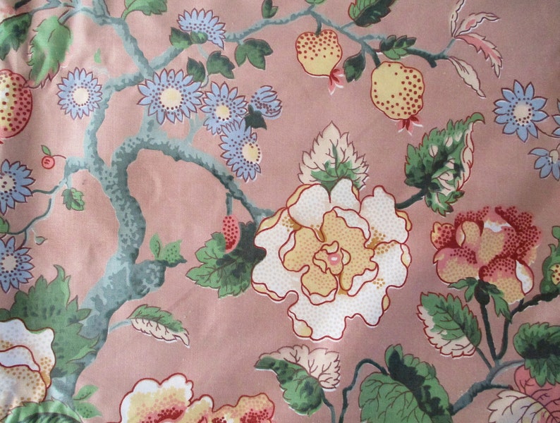 May include: A pink fabric with a floral pattern. The pattern features white, yellow, and red flowers with green leaves. There are also small blue flowers and red berries.