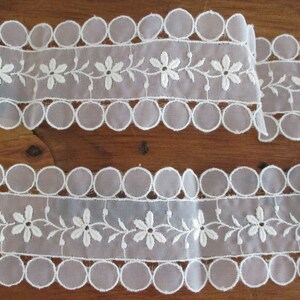 May include: Two pieces of white lace trim with scalloped edges and embroidered floral designs.