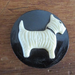 Puede incluir: Un botón de plástico blanco con una imagen en relieve de un perro. El perro está de pie sobre un fondo negro.