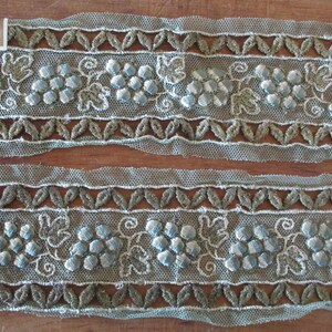 May include: Two pieces of light blue and green embroidered lace trim with a grape motif. The trim is approximately 1 1/2 inches wide.