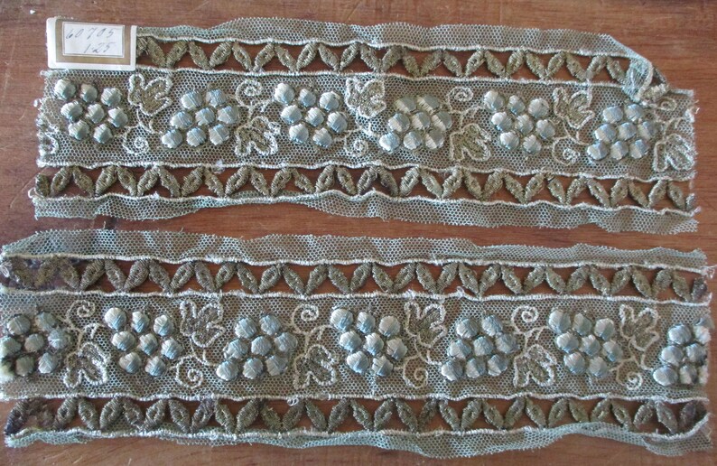 May include: Two pieces of light blue and green embroidered lace trim with a grape motif. The trim is approximately 1 1/2 inches wide.
