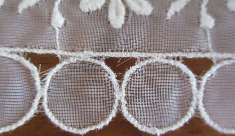 May include: White lace trim with a scalloped edge and a delicate floral pattern.