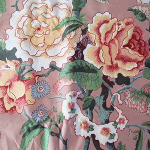 May include: A pink fabric with a floral pattern featuring large white, yellow, and red roses with green leaves. The fabric has a vintage aesthetic.