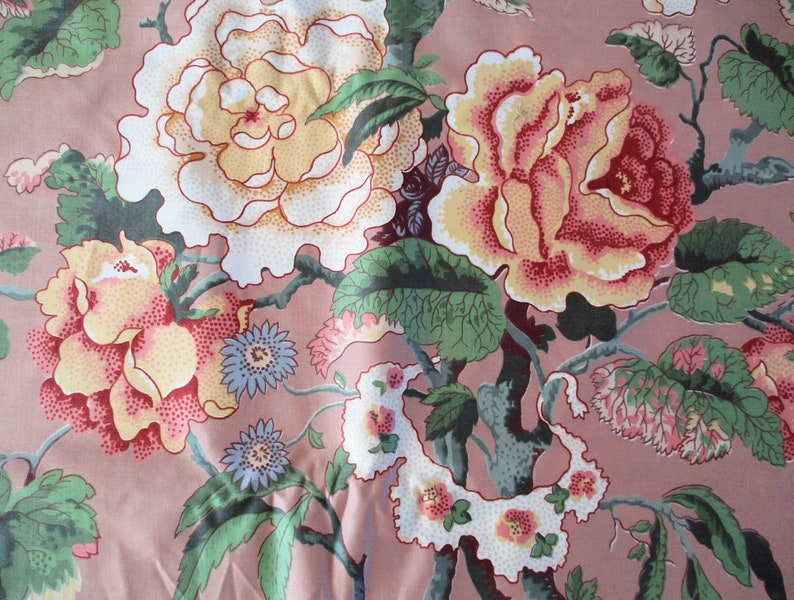May include: A pink fabric with a floral pattern featuring large white, yellow, and red roses with green leaves. The fabric has a vintage aesthetic.