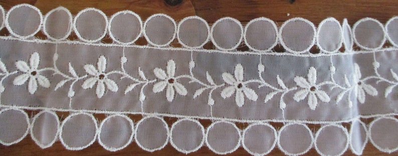 May include: White lace trim with a scalloped edge and a delicate floral design.