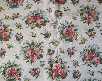 May include: A white fabric with a repeating pattern of pink and red roses, green leaves, and blue flowers. The background has a subtle diamond pattern.