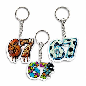 Può includere: Tre portachiavi con il numero "67" in stile graffiti. Uno presenta un pallone da basket, un altro un pallone da calcio e il terzo un design colorato con un berretto da baseball. Ogni portachiavi ha una catena e un anello argentati.