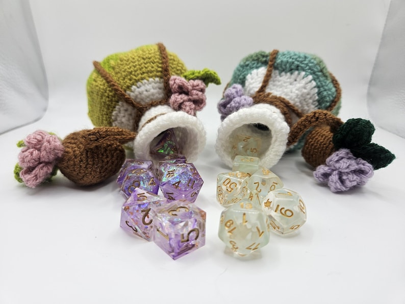 Two green crocheted potion bottle dice bag pouches spill two sets of polyhedral gaming dice onto a flat surface