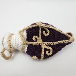 A flattened crochet Royal potion bottle dice bag lays on a flat sruface.