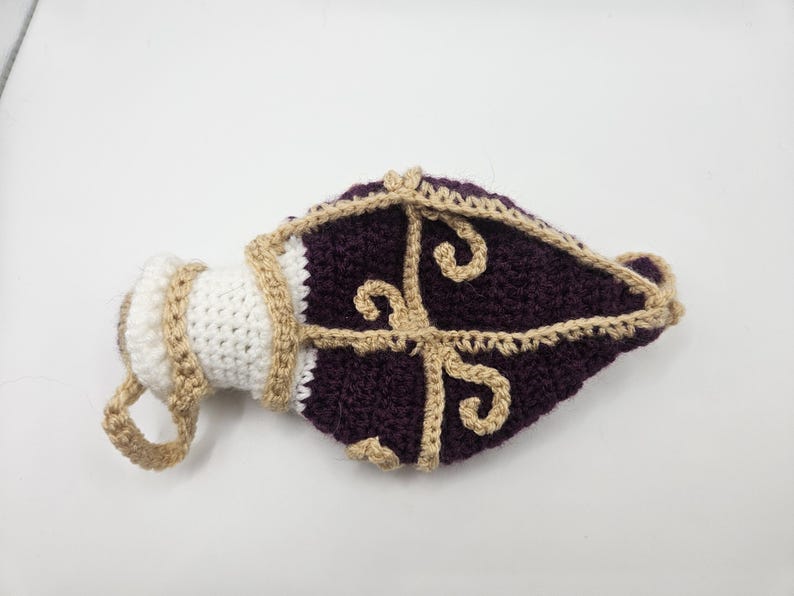A flattened crochet Royal potion bottle dice bag lays on a flat sruface.