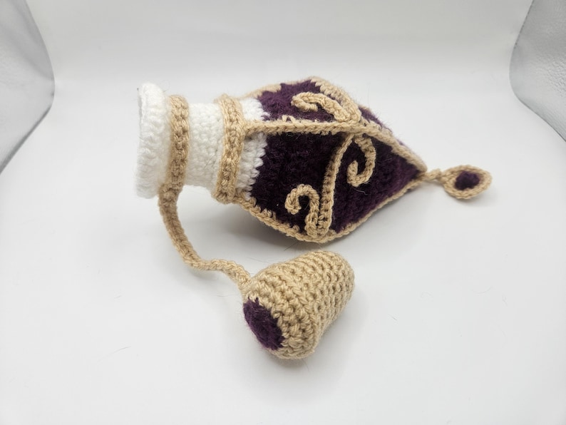 Laying on a flat surface the Royal crochet potion bottle dice bag with the cork to one side.