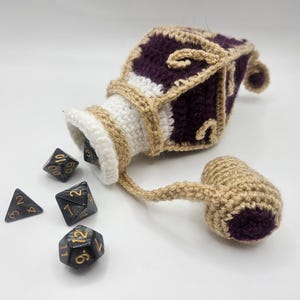 Polyhedral gaming dice spill out of a diamond shaped crocheted purple potion bottle dice bag, gaming pouch, accessory