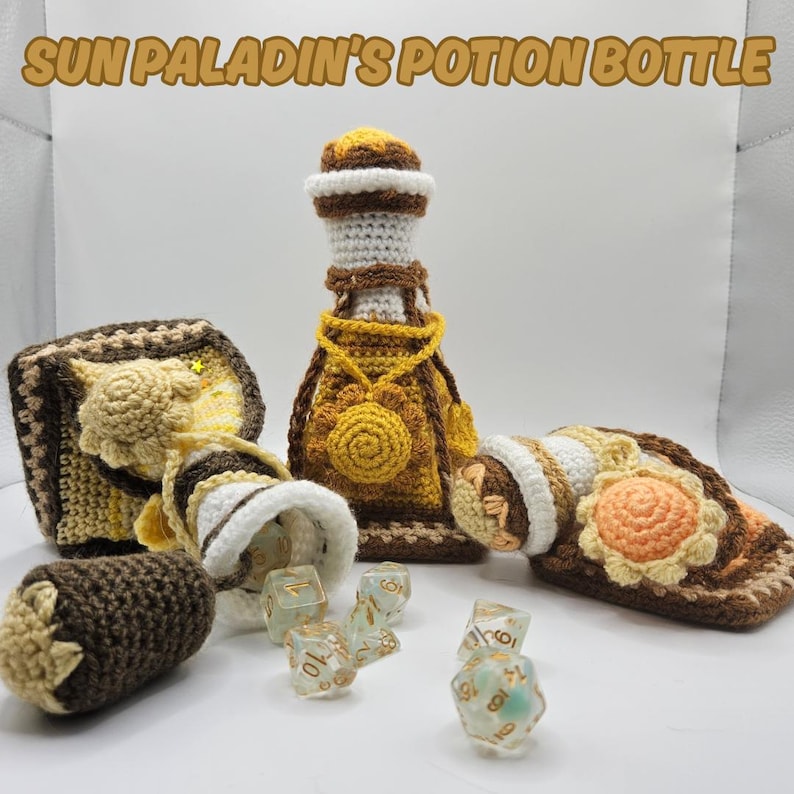 Text reads: Sun Paladin's Potion Bottle.
Three yellow crocheted potion bottles in slightly different colours. The leftmost bottle is the lightest, it is lying on its side, with the cork pulled out and light coloured polyhedral gaming dice often used in table top gaming or TTRPG are spilling out of it. A dark yellow potion bottle stands tall in the middle with a sun charm around its neck. A yellow and light orange potion bottle is squashed / flattened on the right.