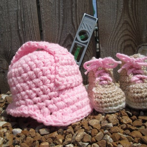 May include: Pink crocheted hat with a brim and two pairs of brown crocheted booties with pink laces.