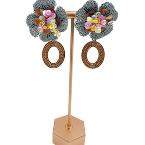 May include: A pair of silver and gold earrings with a flower-shaped design. The flowers are adorned with colourful beads and sequins. The earrings are hanging from a gold stand.