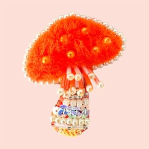 May include: Orange and white beaded mushroom brooch with iridescent sequins.