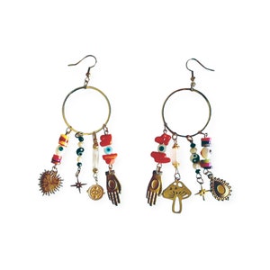 May include: Gold hoop earrings with colourful beads, charms, and pendants. The charms include a sun, a star, a hand, an eye, and a mushroom.