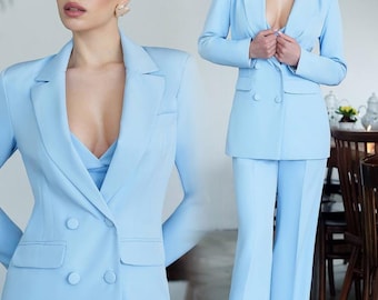 Puede incluir: Un blazer azul claro de doble botonadura y pantalones anchos a juego. El blazer tiene solapa de muesca y dos bolsillos. Los pantalones tienen cintura alta y pierna ancha.