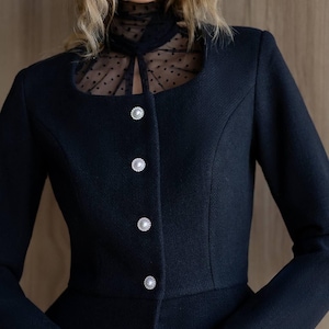 May include: A black blazer with a square neckline and three pearl-like buttons. The blazer features a sheer, polka-dot panel at the neckline. The sleeves are long and the fabric has a textured appearance.