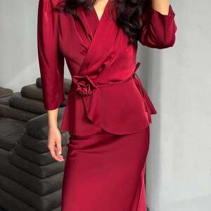 May include: A burgundy satin wrap top with a rose detail at the waist and a matching skirt. The top has a V-neckline and three-quarter sleeves.