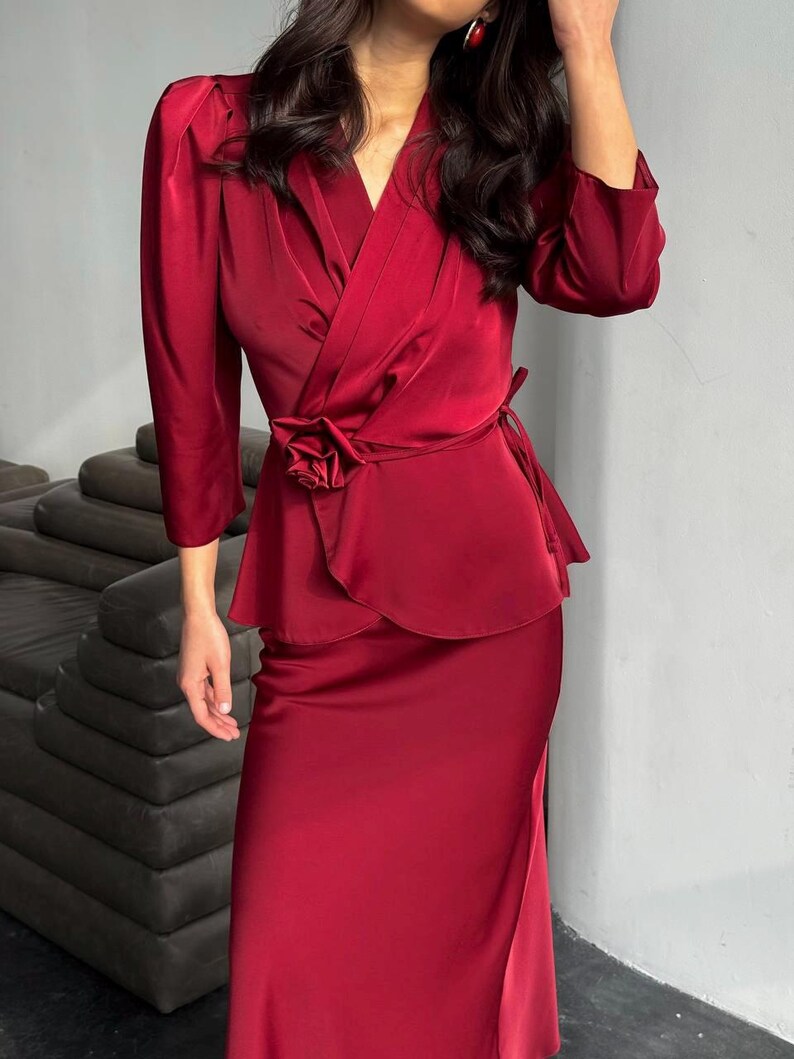 May include: A burgundy satin wrap top with a rose detail at the waist and a matching skirt. The top has a V-neckline and three-quarter sleeves.