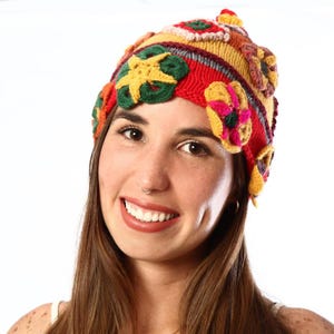 Puede incluir: Un gorro colorido tejido a mano con adornos florales y en forma de estrella. El gorro presenta una vibrante mezcla de tonos rojos, amarillos, verdes y naranjas. Un accesorio único y llamativo.