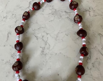 May include: A handmade necklace featuring large, dark brown buckeye nuts interspersed with small red and white beads. The necklace is strung on a flexible cord, creating a circular shape. The buckeyes have a smooth, polished appearance.