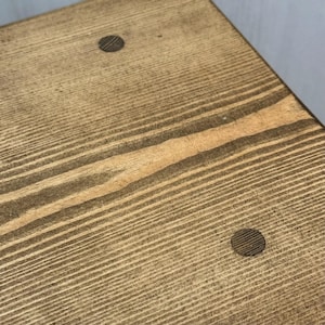 Close-up view of the wooden grain texture on top of a rustic stool showing two circular dowel plugs.