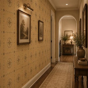 May include: A hallway featuring tan wallpaper with a repeating dark compass rose pattern, dark wood framed landscape art, a long beige runner rug, and a wooden console table holding a ceramic vase with greenery and stacked books.