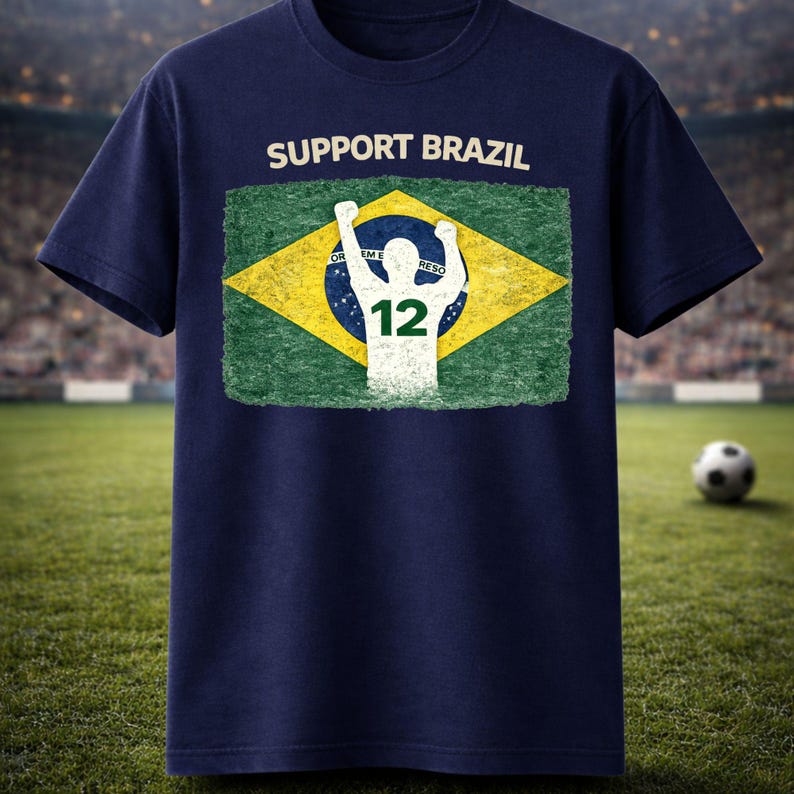 Puede incluir: Camiseta azul marino con el texto "SUPPORT BRAZIL" sobre una bandera brasile&ntilde;a desgastada. El dise&ntilde;o de la bandera incluye una silueta blanca de una persona con los brazos levantados y el n&uacute;mero 12.