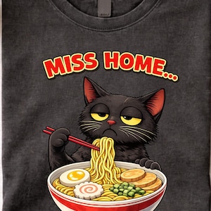 May include: Dark grey t-shirt with a black cat illustration eating ramen from a red and white bowl. The text "MISS HOME..." is above the cat in red and yellow.