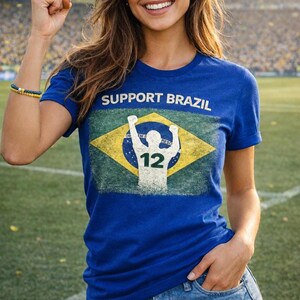 Puede incluir: Una camiseta azul con la frase "SUPPORT BRAZIL" sobre un dise&ntilde;o desgastado de la bandera brasile&ntilde;a. El gr&aacute;fico incluye una silueta de persona con los brazos levantados y el n&uacute;mero "12". La camiseta la lleva una persona.