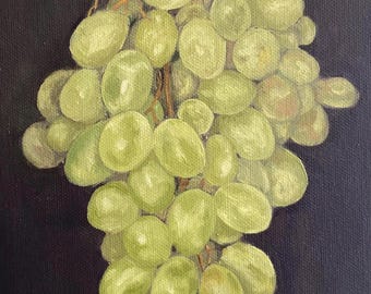 May include: A bunch of green grapes hanging from a vine against a dark background. The grapes are clustered together and have a slightly yellowish hue.