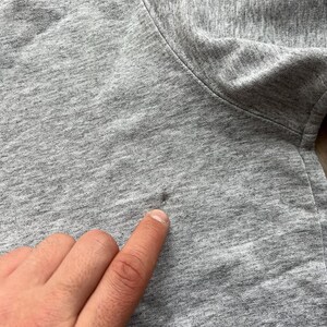 May include: Close-up of a grey sweatshirt with a small hole in the fabric.
