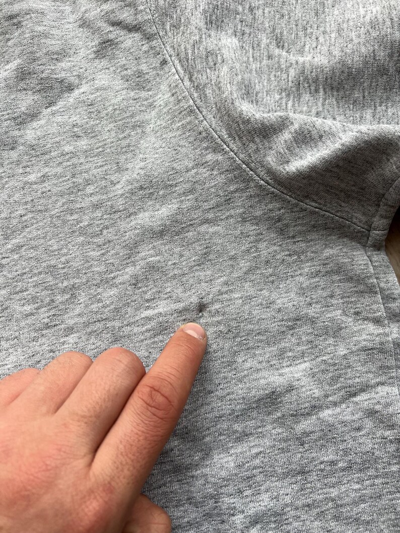 May include: Close-up of a grey sweatshirt with a small hole in the fabric.