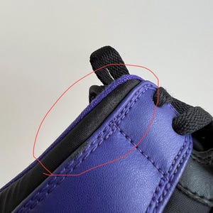 May include: Close-up of a purple and black shoe with a black strap. The shoe has a stitched seam around the edge of the purple leather.