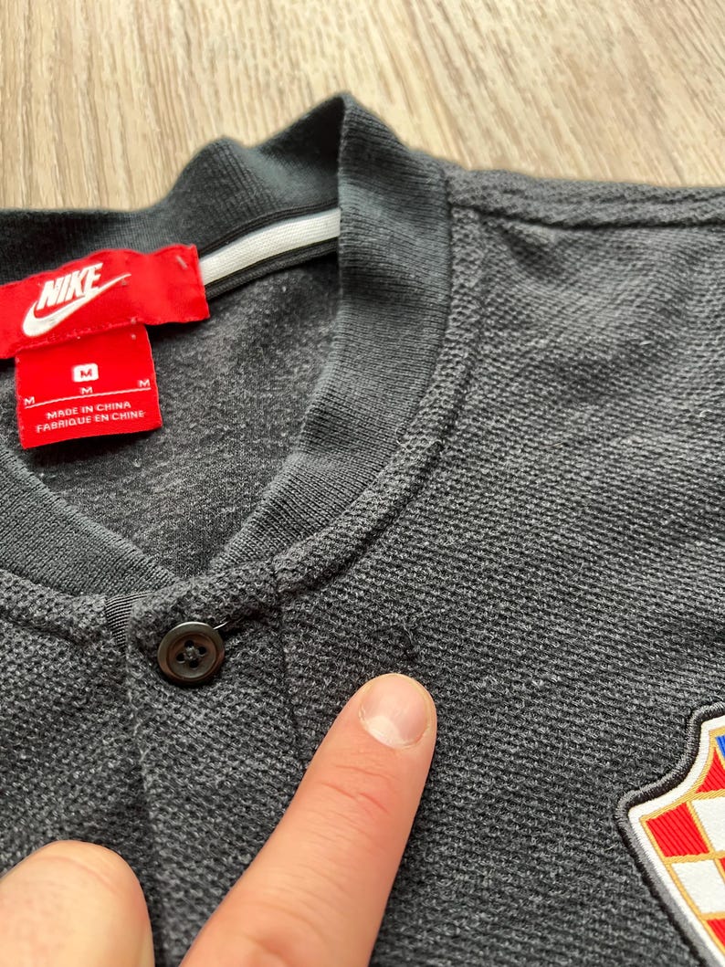May include: A gray polo shirt with a black button and a Nike logo on the left chest. The shirt has a white tag with the text "Made in China Fabrique en Chine" and the size "M".