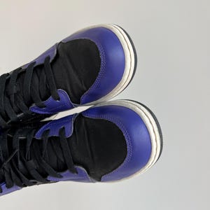 May include: A pair of high-top sneakers with black canvas uppers and purple leather accents. The shoes have white soles and black laces.