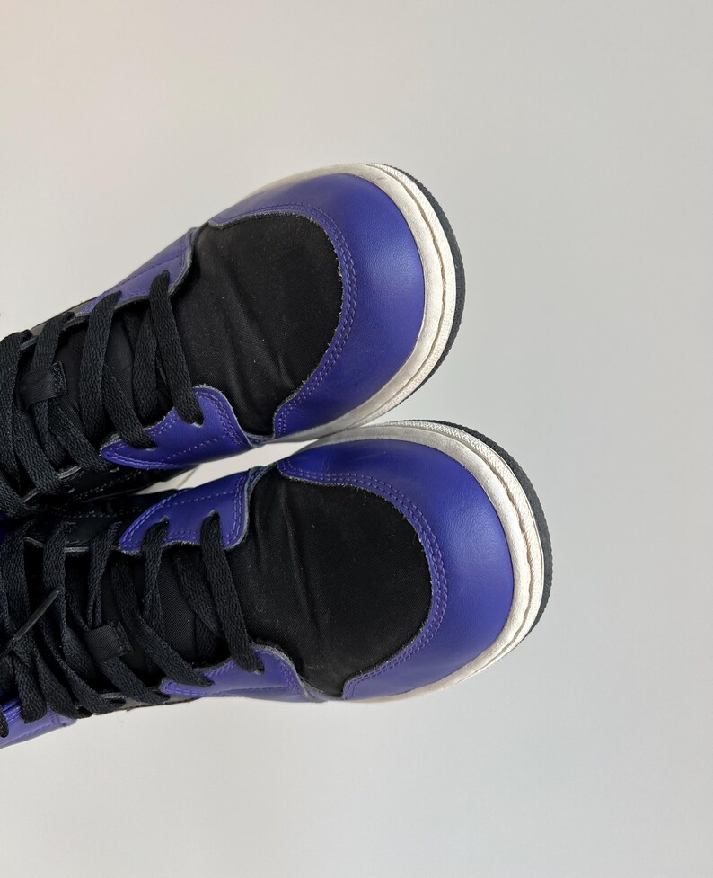 May include: A pair of high-top sneakers with black canvas uppers and purple leather accents. The shoes have white soles and black laces.