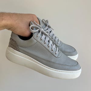 Può includere: Sneakers basse in pelle grigia con lacci bianchi e suola in gomma bianca.