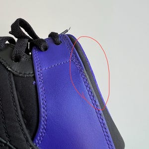 May include: Close-up of a black and purple sneaker with a visible seam along the side. The seam is slightly frayed.