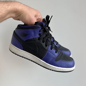 May include: Black and purple mid-top sneakers with a white sole and black laces. The Nike Air Jordan logo is visible on the side of the shoe.
