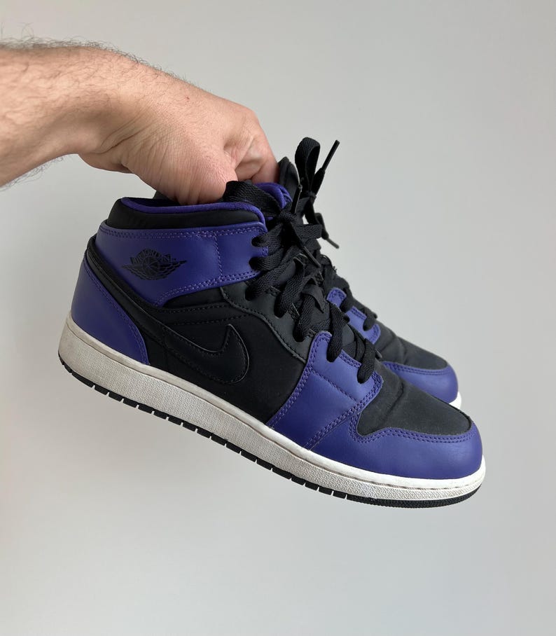 May include: Black and purple mid-top sneakers with a white sole and black laces. The Nike Air Jordan logo is visible on the side of the shoe.