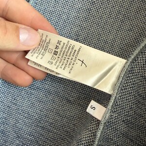 May include: A blue and white textured knit garment featuring a white fabric care label with the text Made in Italy and a small separate white tag with the letter S. The label includes various laundry symbols and multilingual instructions.