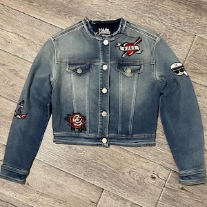 May include: A blue denim jacket with a variety of embroidered patches, including a heart with the word "Karl" inside, a rose, an anchor, and a cartoon face with sunglasses.