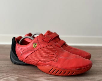 May include: Red and black athletic shoes with a textured design and a hook-and-loop strap. The shoes have a low profile and a rubber sole. A yellow Ferrari logo is visible on the side.